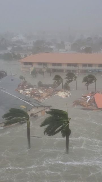 This may contain: a building surrounded by flood waters with palm trees in the foreground and buildings on either side