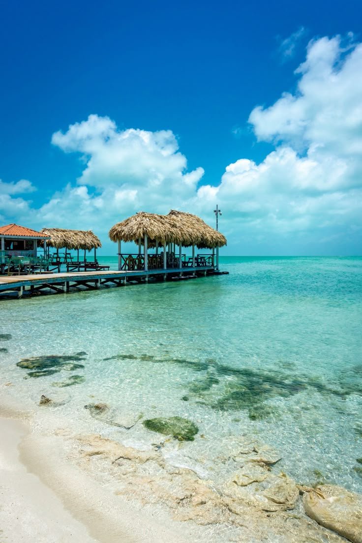 This may contain: the water is crystal blue and clear with some straw umbrellas on it's roof
