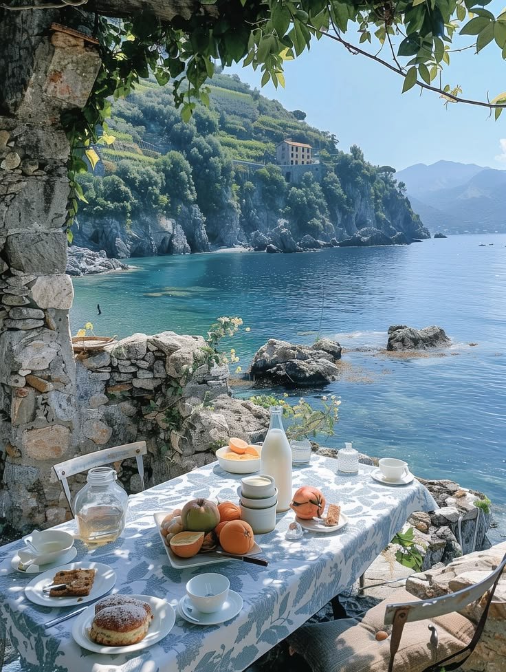 This may contain: an outdoor table with food on it next to the ocean