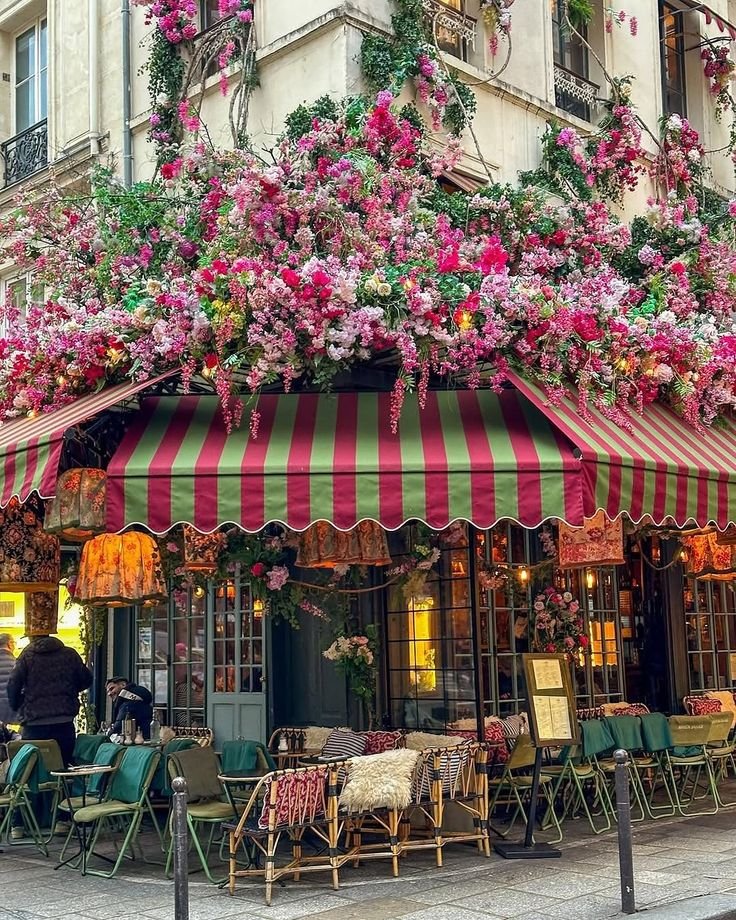 This may contain: an outdoor cafe with flowers on the roof and awnings over it's tables