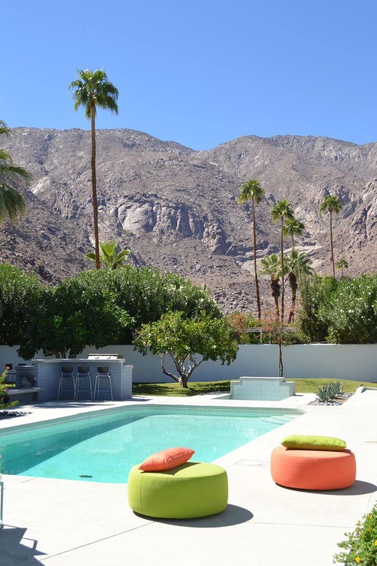 This may contain: an outdoor pool surrounded by palm trees with mountains in the background and two lounge chairs