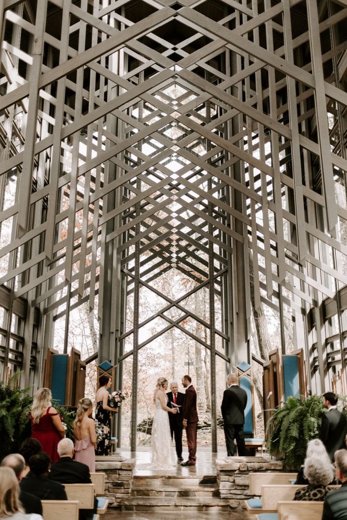 This may contain: a couple getting married in front of an open air structure with people sitting on the pews
