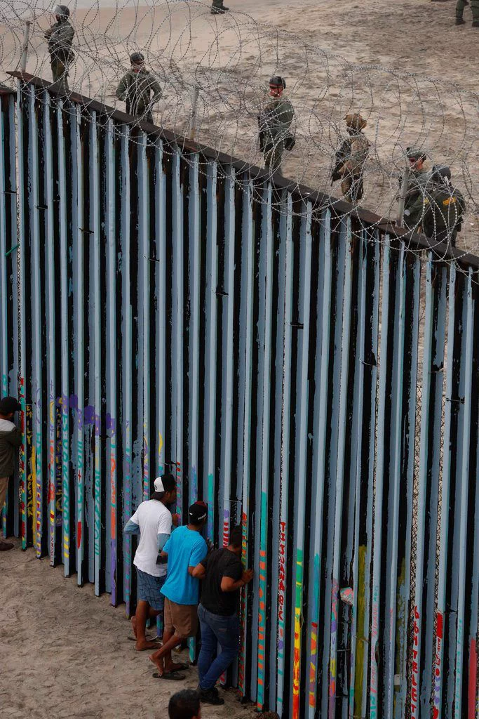 This may contain: several people are standing on the side of a wall with barbed wire and looking over it