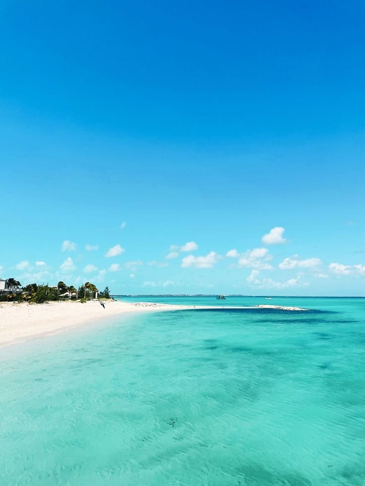 This may contain: the water is very clear and blue with white sand on the beach in front of it