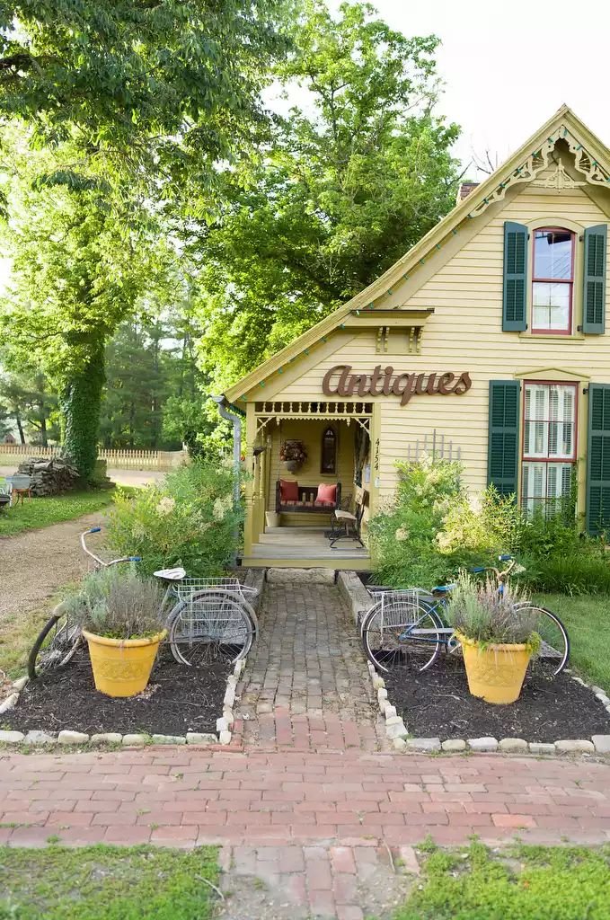This may contain: a small yellow building with green shutters on the front and two bicycles parked outside