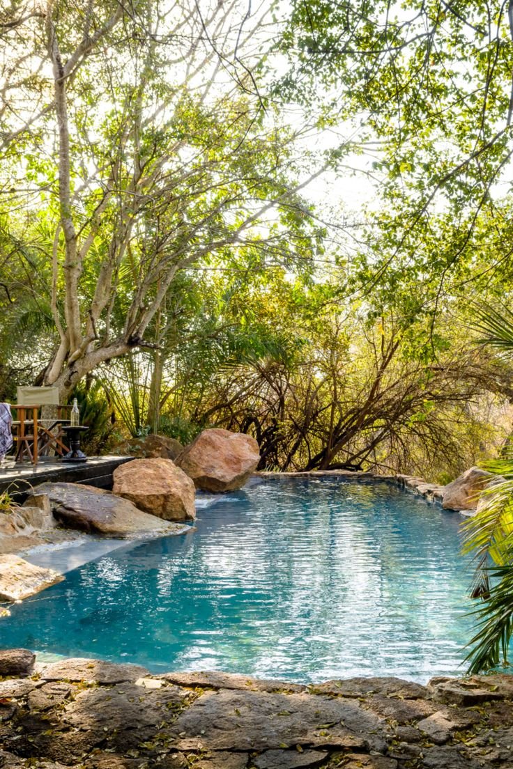 This may contain: an outdoor swimming pool surrounded by trees and rocks