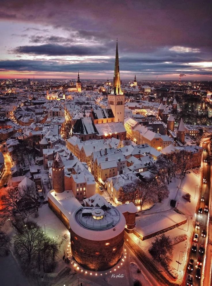 This may contain: an aerial view of a city at night with snow on the ground and buildings lit up