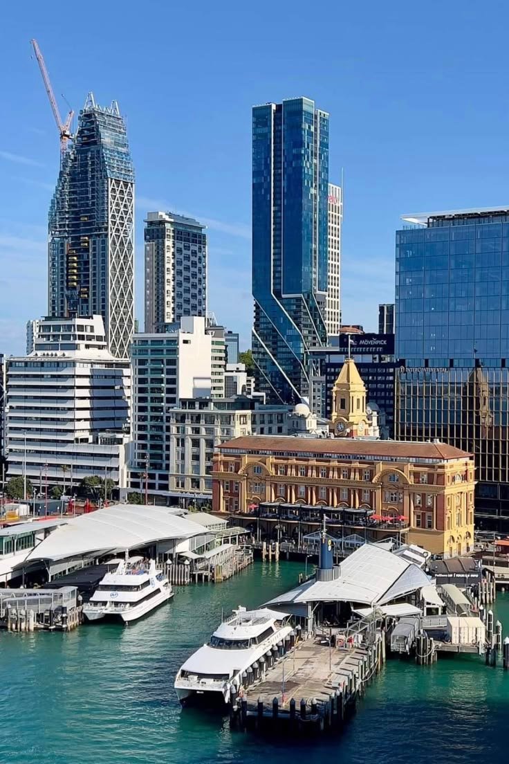 This may contain: the city is full of tall buildings and some boats are docked on the water in front of them