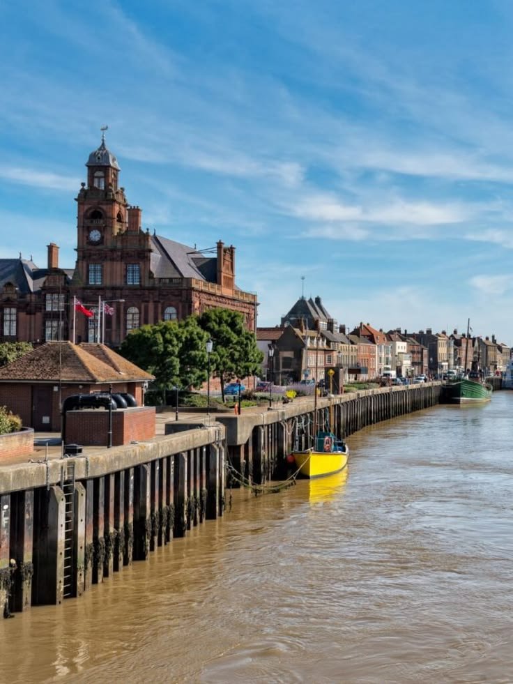 This may contain: a yellow boat floating on top of a river next to a wooden pier with buildings in the background