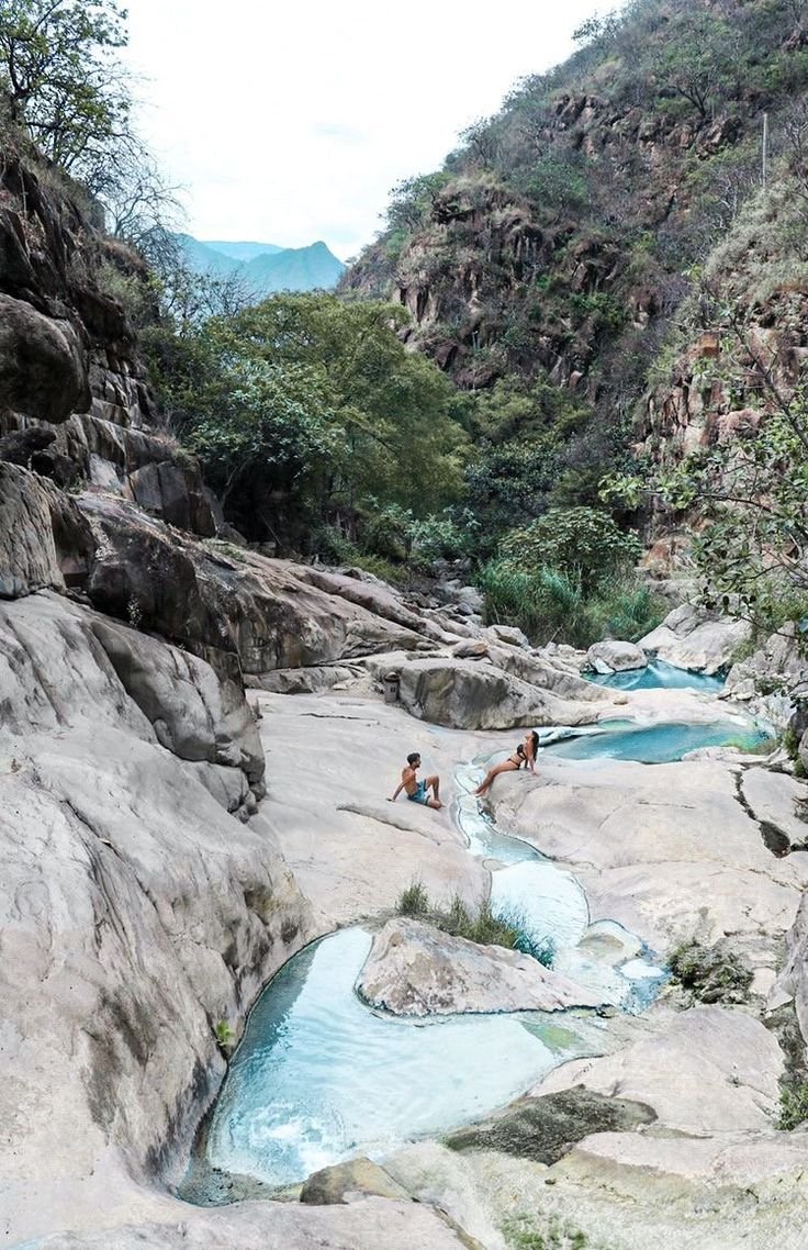 This may contain: two people are sitting on the rocks near a river that is running through some mountains