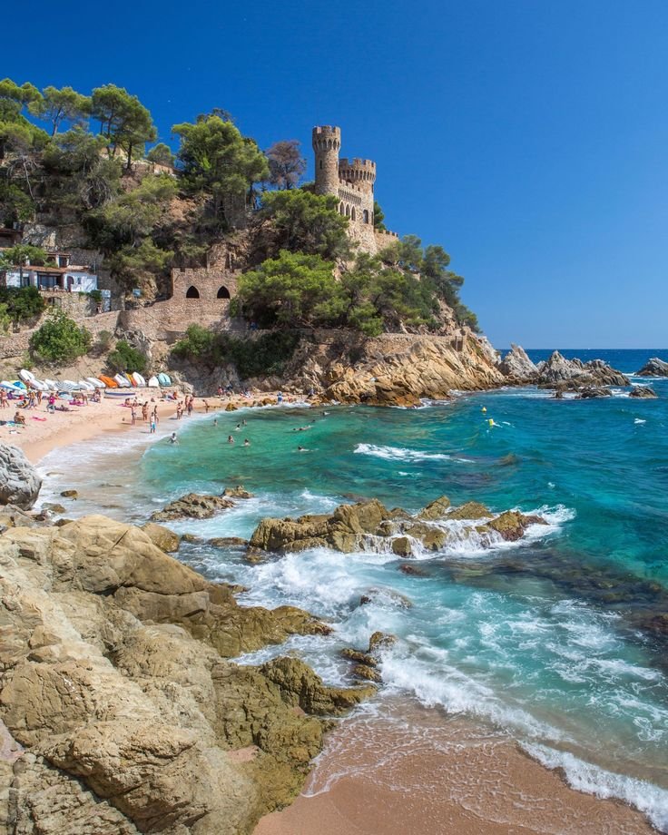 This may contain: people are on the beach and in the water near an old castle that is perched on top of a hill