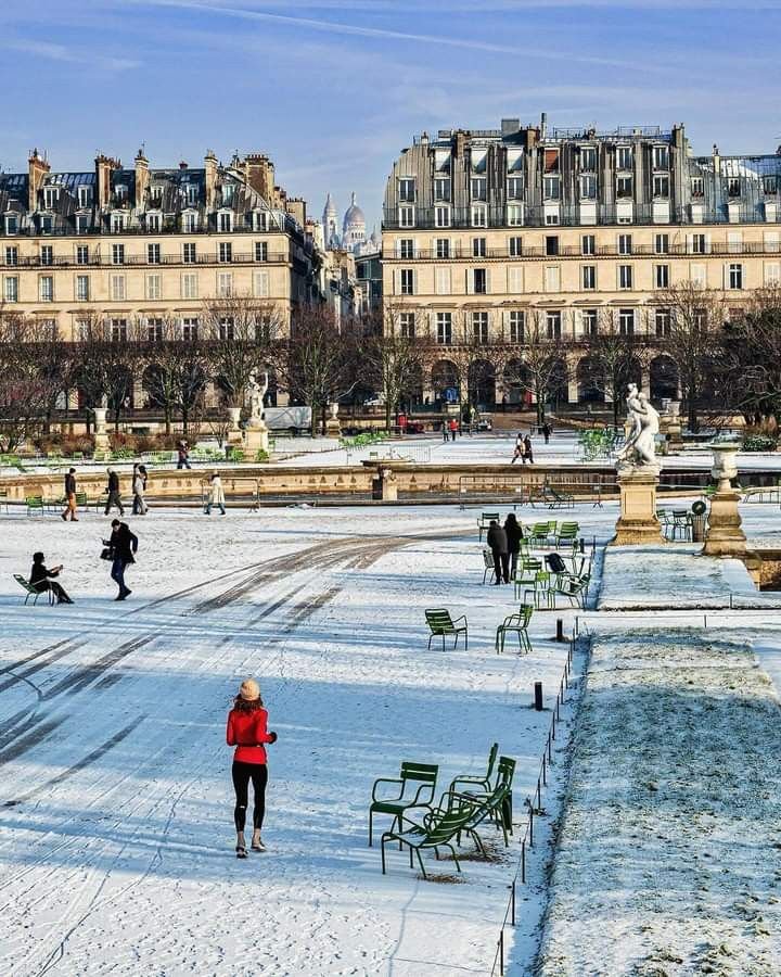 This may contain: people are walking around in the snow near some buildings and benches with no one on them
