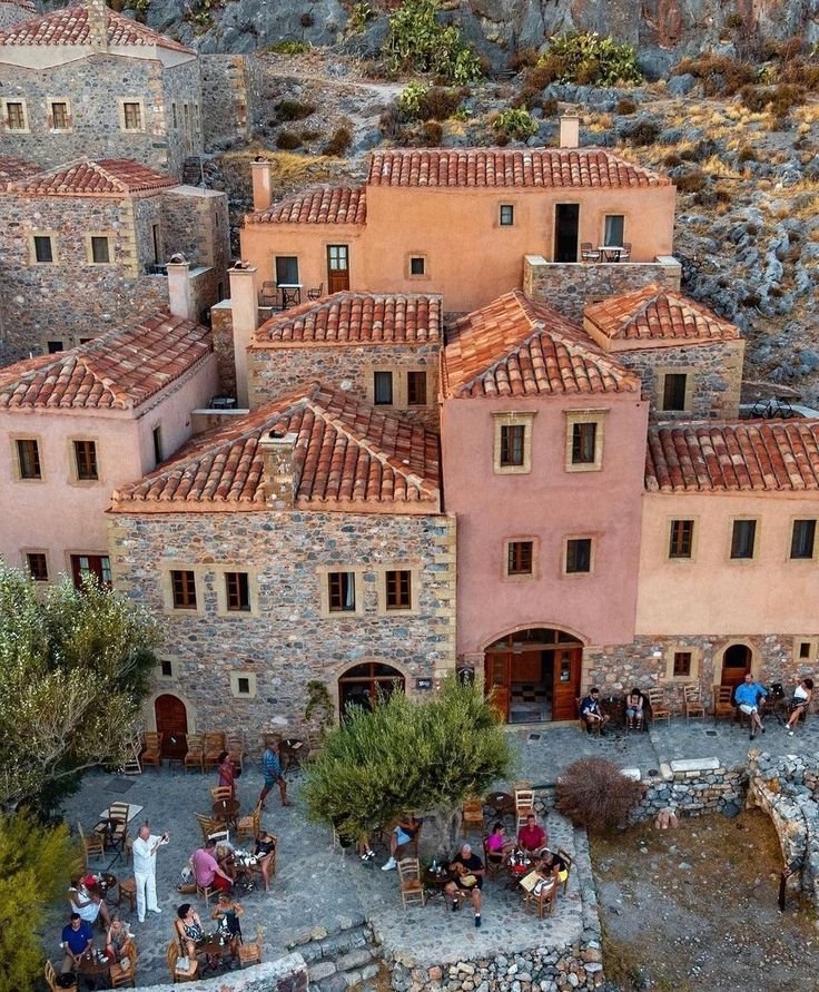 This may contain: an aerial view of people sitting at tables in front of stone buildings with red tiled roofs