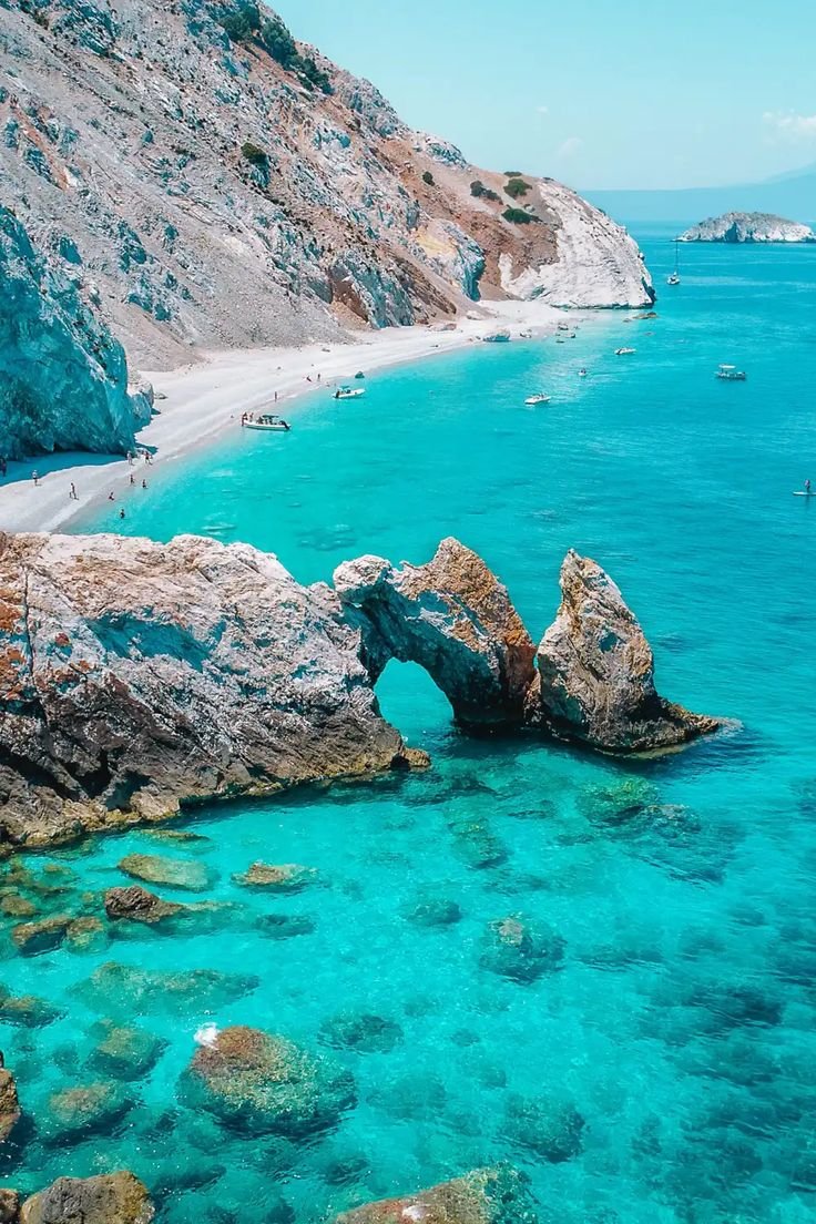 This may contain: the water is crystal blue and clear with people swimming in it on the rocks near the beach