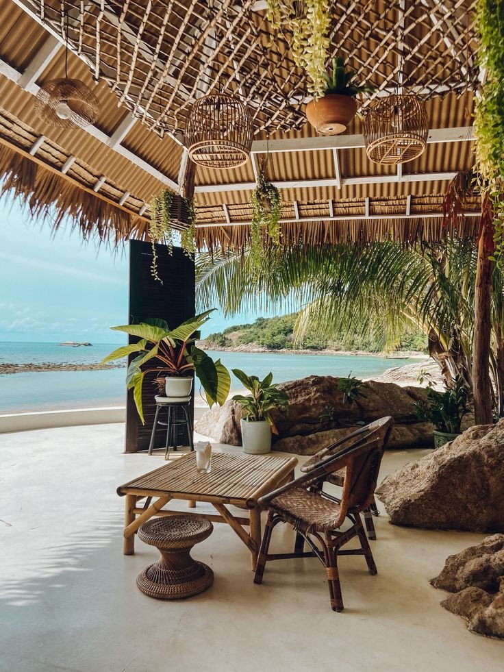This may contain: a table and chairs under a thatched roof next to the ocean