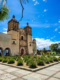 This may contain: an old building with many plants in front of it and blue skies above the buildings