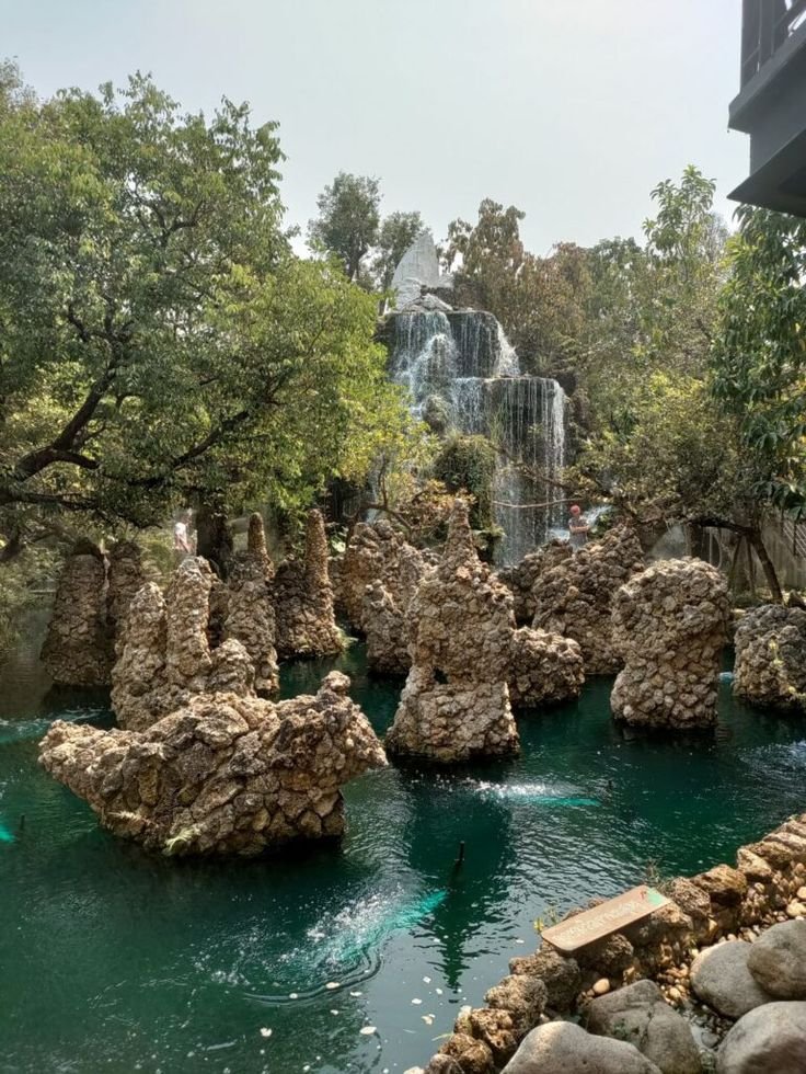 This may contain: there are many rocks in the water and some people swimming under them at the waterfall