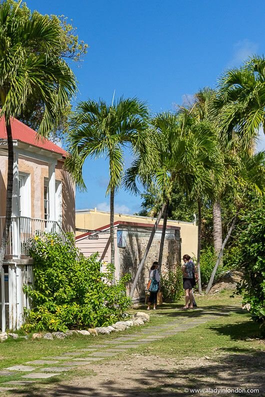 This may contain: two people walking down a path between palm trees in front of an old pink building