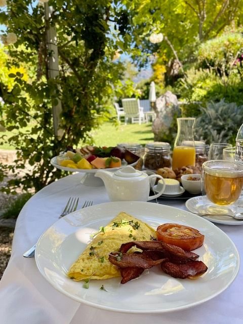 This may contain: an outdoor table with breakfast food and drinks on it, including eggs, bacon, tomatoes, and toast