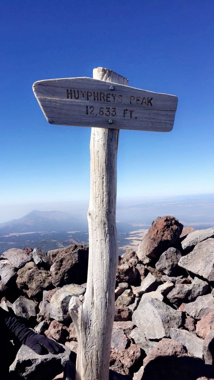 This may contain: a wooden sign sitting on the side of a mountain