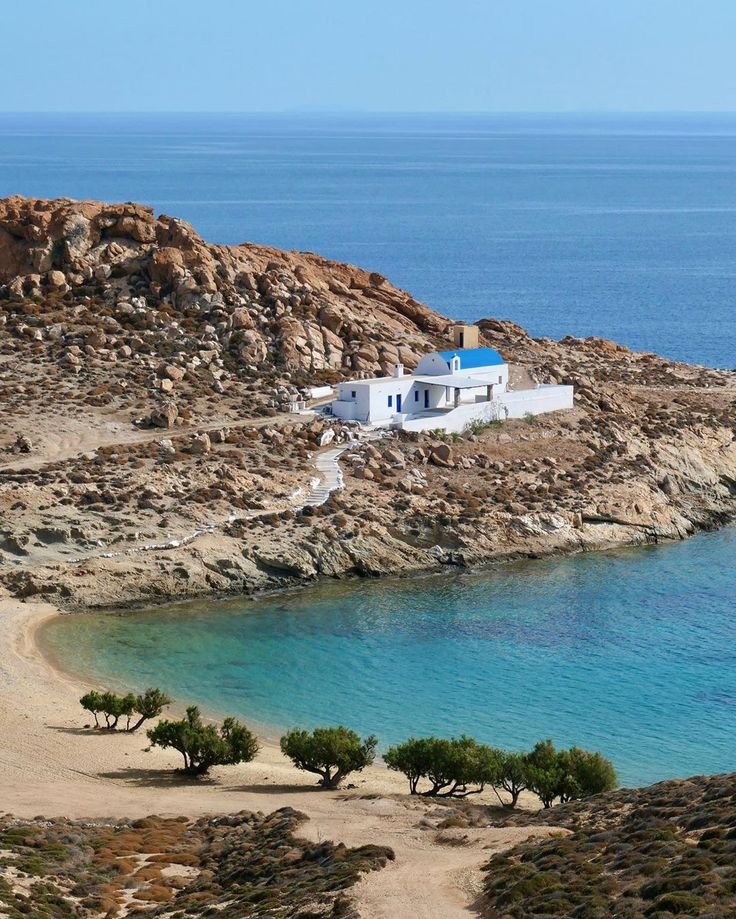 This may contain: a white house sitting on top of a rocky hill next to the ocean with blue water