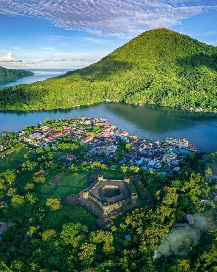This may contain: an aerial view of a small village in the middle of a lake surrounded by lush green hills