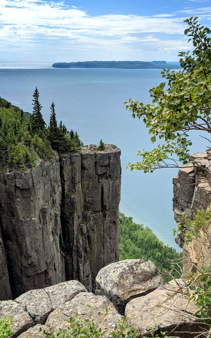 This may contain: a view of the ocean and trees from an overlook point on top of a cliff
