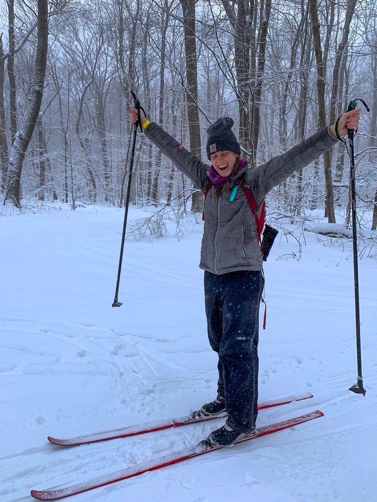 This may contain: a woman on skis standing in the snow with her arms up and hands raised