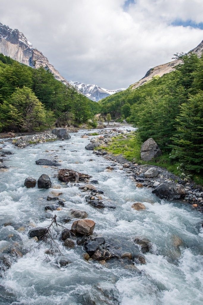 This may contain: a river running through a lush green forest filled with rocks and water surrounded by mountains