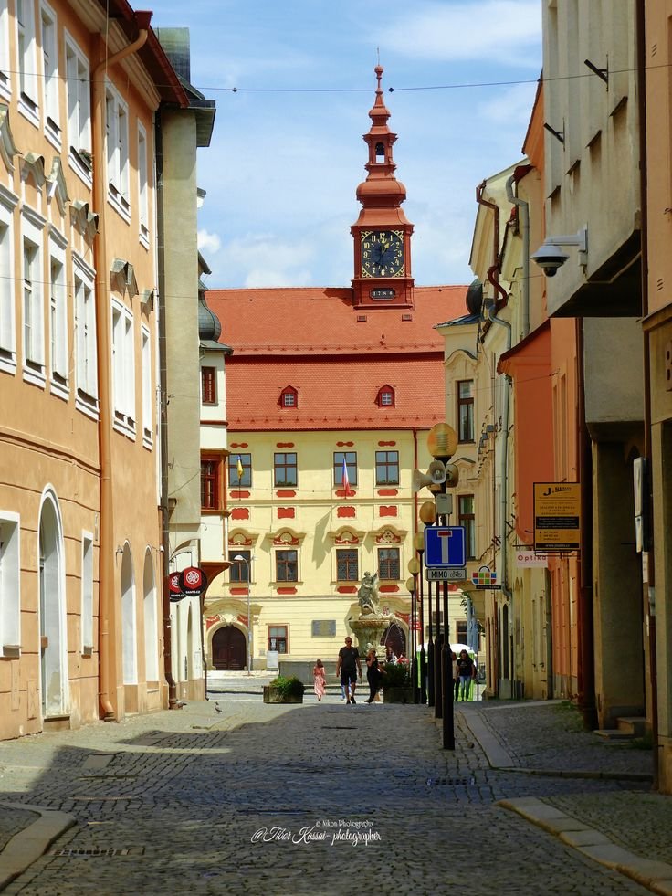 This may contain: a clock tower on top of a building in the middle of an alley way with people walking down it