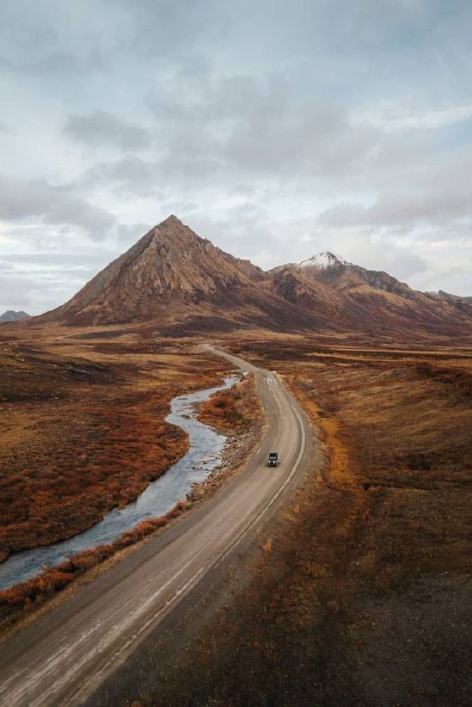 This may contain: an aerial view of a road in the middle of nowhere with mountains in the background