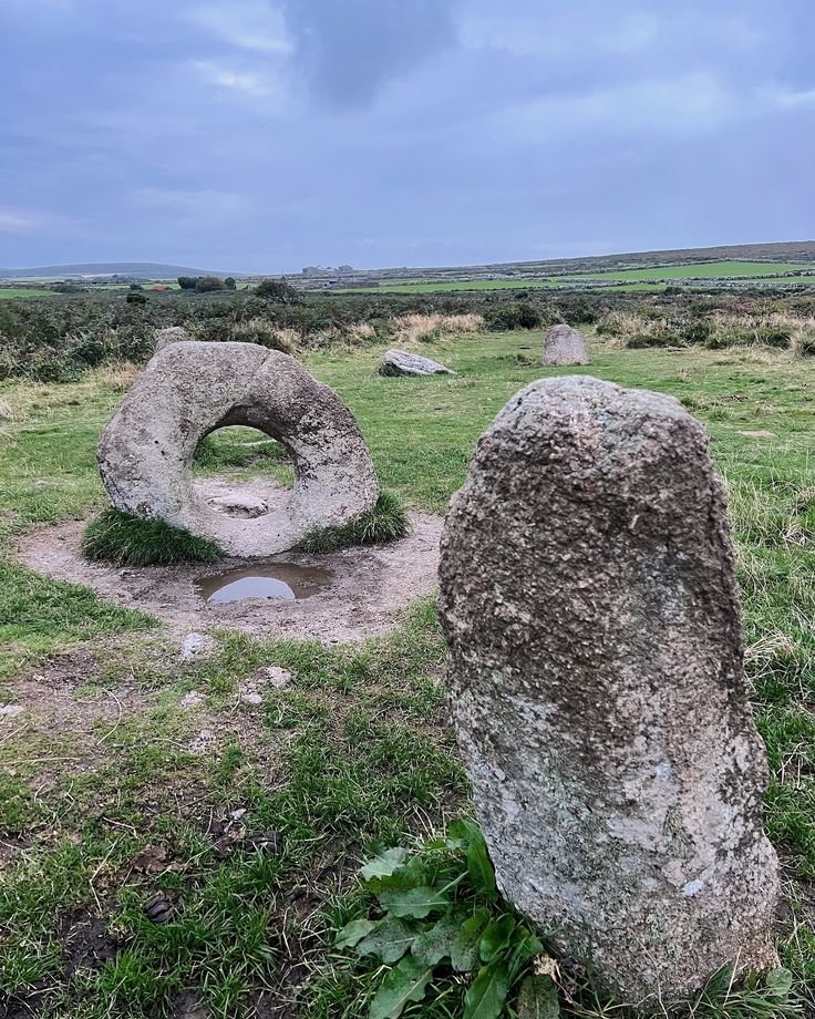 This may contain: two large rocks sitting on top of a lush green field next to a stone circle