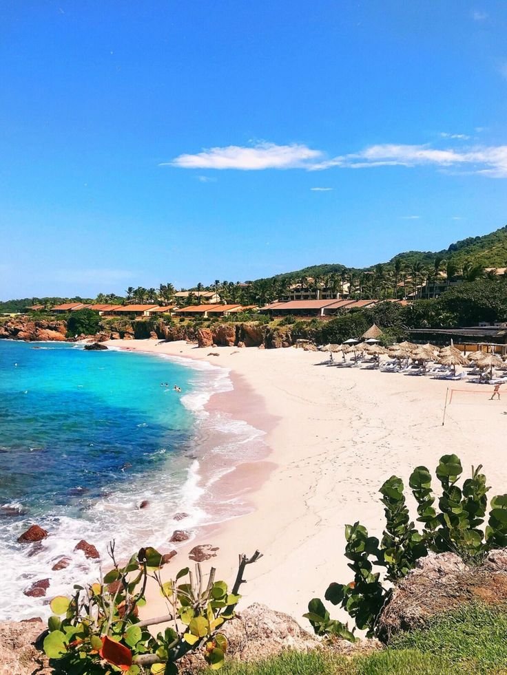 This may contain: a sandy beach next to the ocean under a blue sky