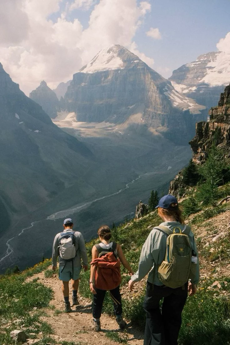 This may contain: three people walking up a hill with mountains in the background