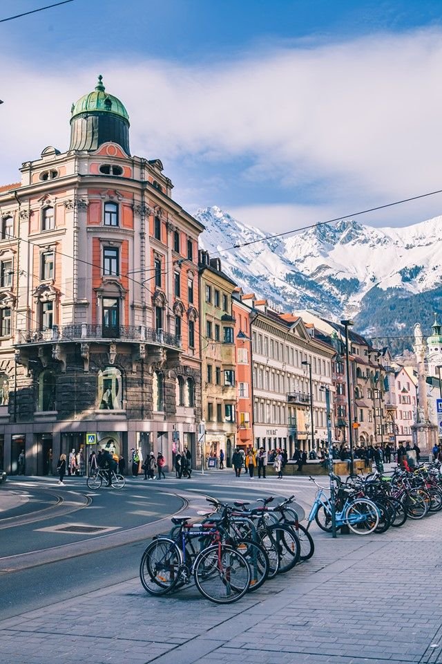 This may contain: many bicycles are parked on the side of the road in front of buildings with mountains in the background