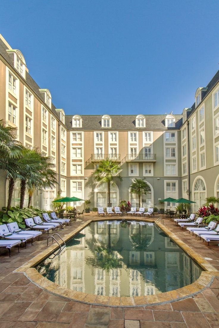 This may contain: an outdoor swimming pool with lounge chairs and palm trees in the foreground, surrounded by tall buildings