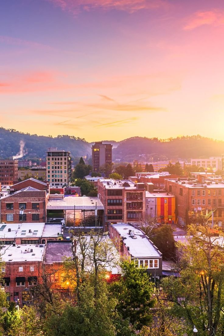 This may contain: the sun is setting over a city with tall buildings and trees in front of it