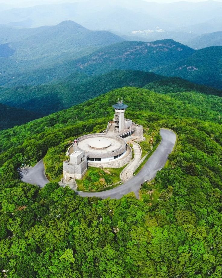 This may contain: an aerial view of a large building in the middle of a forest with mountains in the background