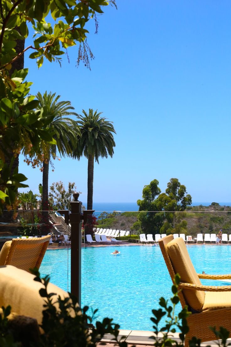 This may contain: two yellow chairs sitting next to each other near a swimming pool with palm trees in the background