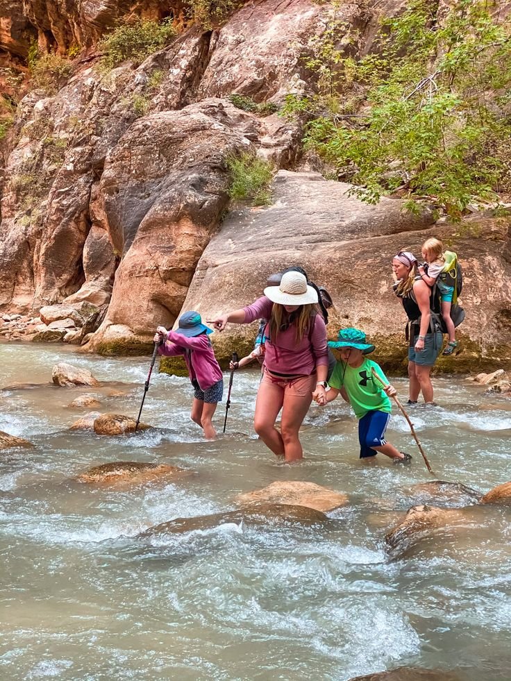 This may contain: several people are crossing a river in the mountains with backpacks and walking sticks on their backs