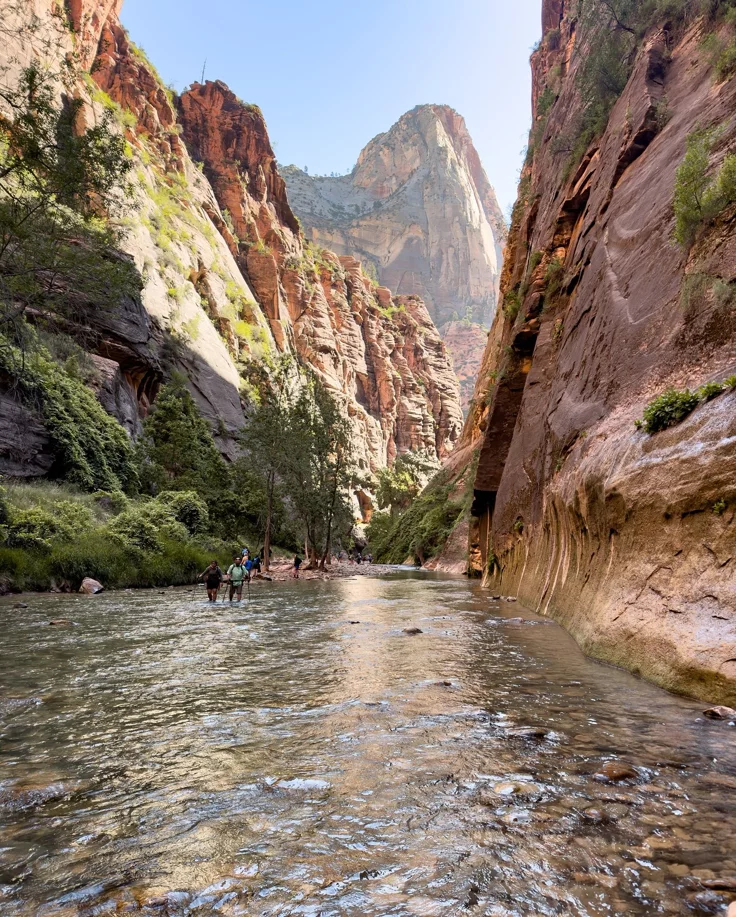 This may contain: people are wading through the water in a narrow canyon with mountains in the background