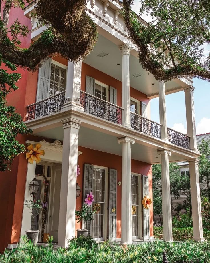 This may contain: an orange house with white columns and balconies on the second floor is surrounded by greenery