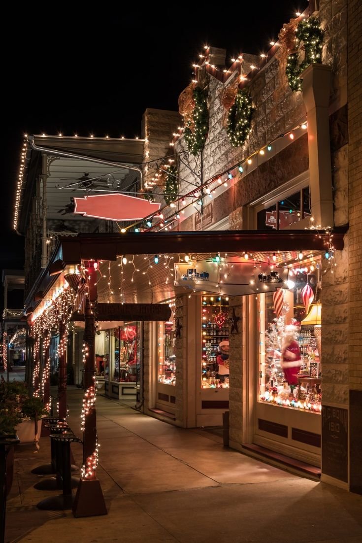 This may contain: a street with christmas lights and decorations on the side of it's buildings at night