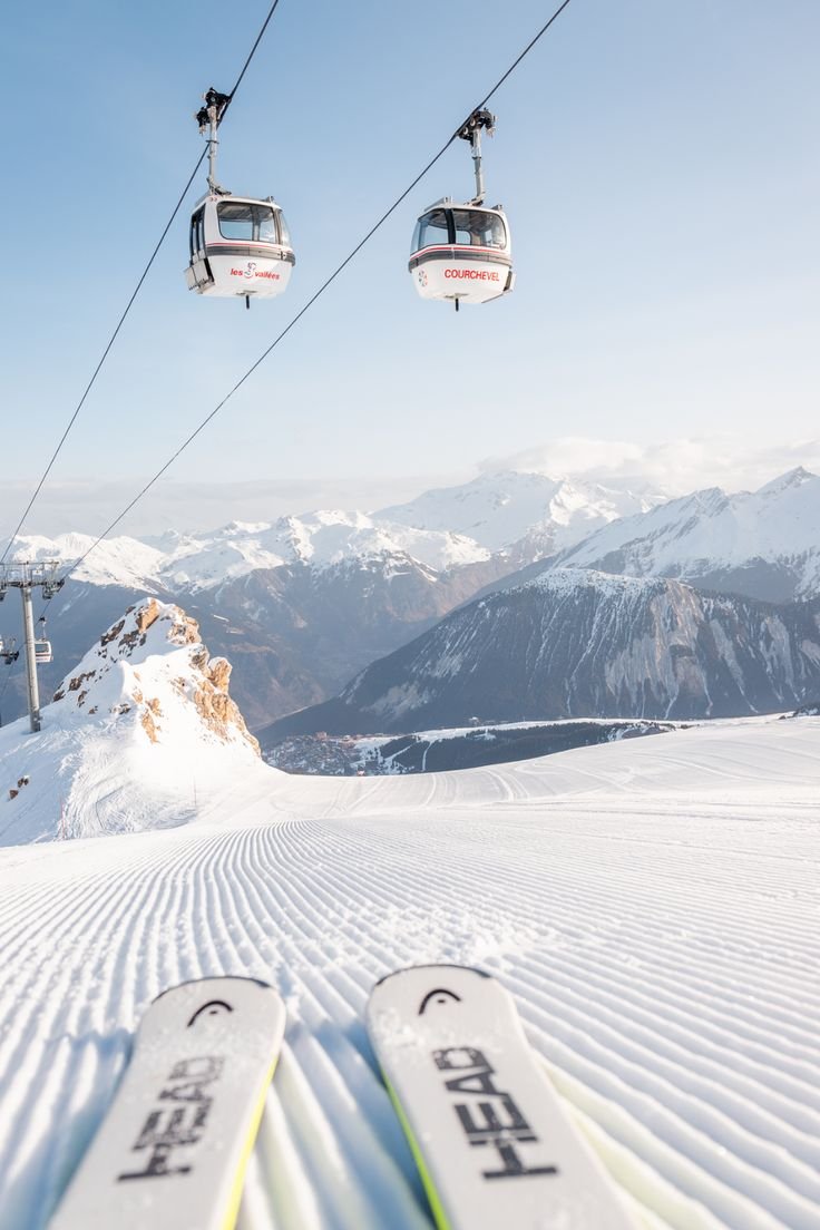 This may contain: two skis sitting in the snow under a chair lift with mountains in the background