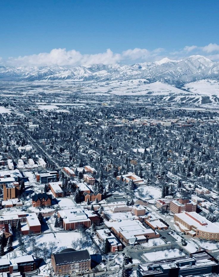 This may contain: the city is covered in snow and surrounded by mountains, trees, and hills with no clouds