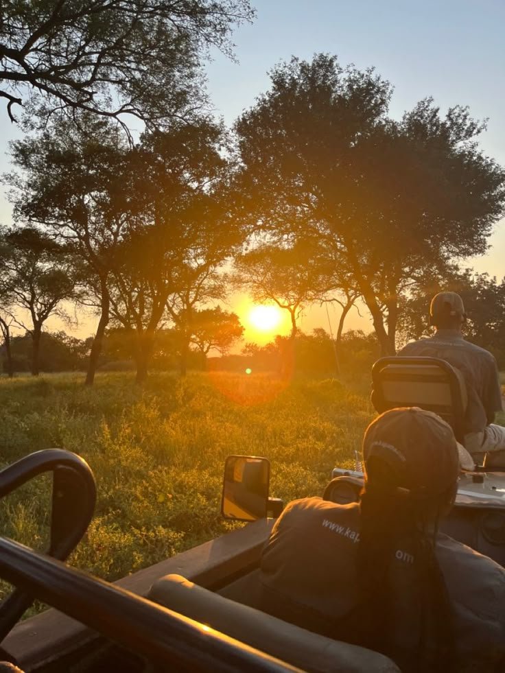 This may contain: the sun is setting behind two people on their atvs in front of some trees