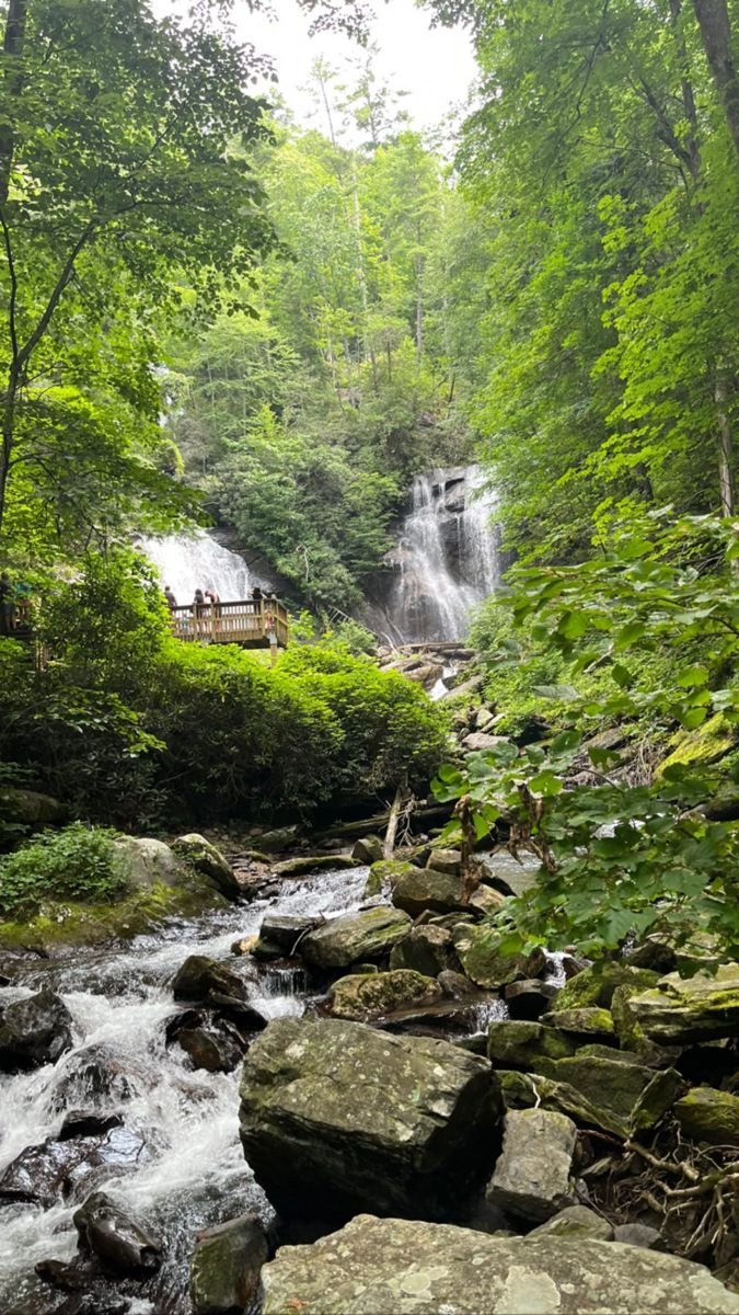 This may contain: a small waterfall in the middle of a forest with lots of rocks and trees around it