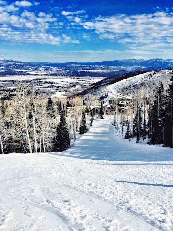 This may contain: a snow covered ski slope with trees and mountains in the background