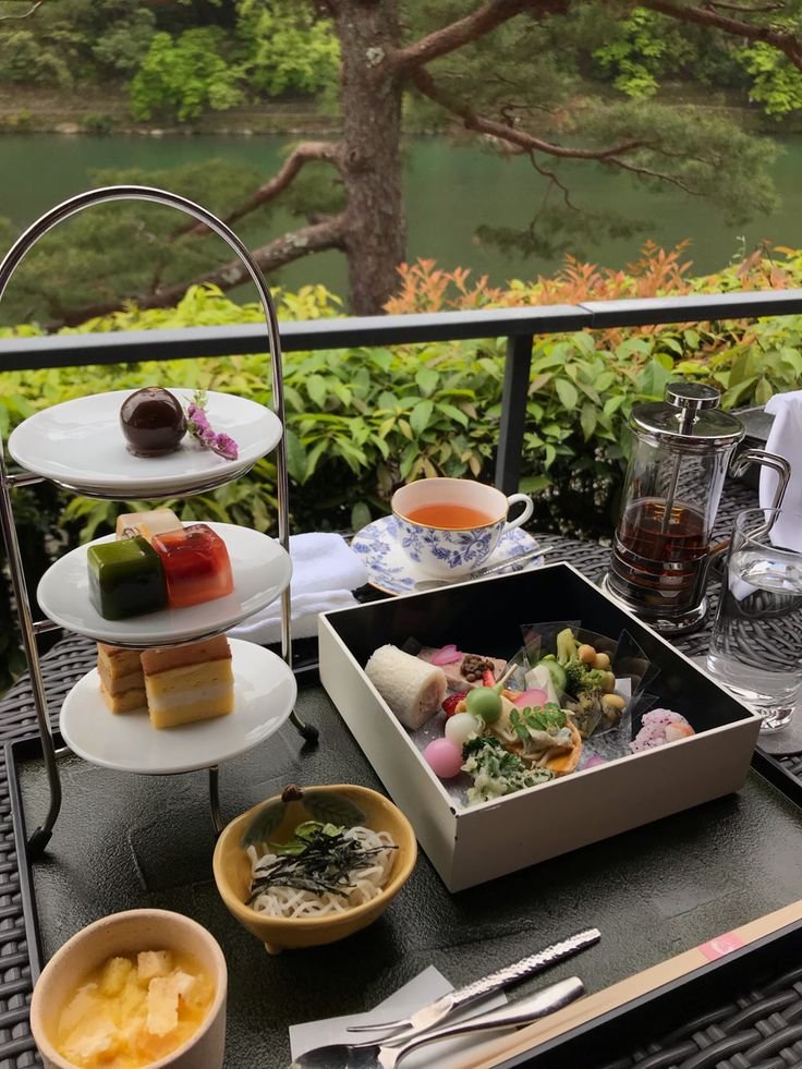 This may contain: an outdoor table with food and drinks on it in front of a tree, overlooking the water