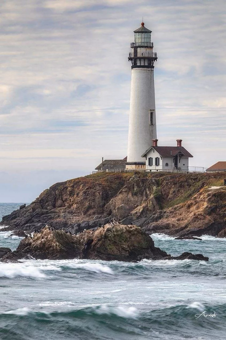 This may contain: a light house sitting on top of a rocky cliff next to the ocean with waves crashing in front of it